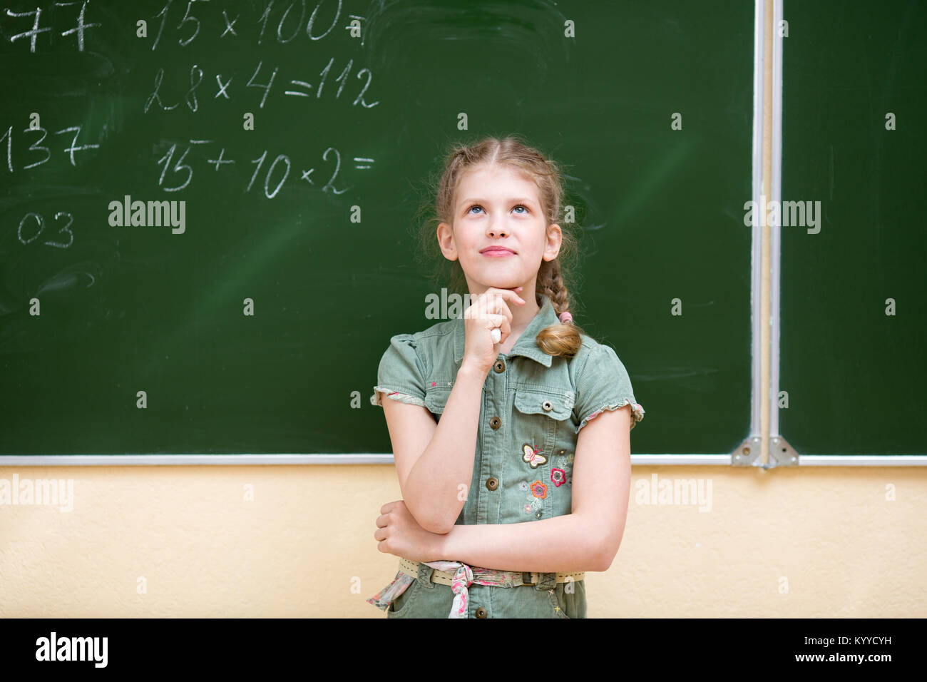 Schoolgirl in aula in piedi alla lavagna risolve un esempio matematico Foto Stock