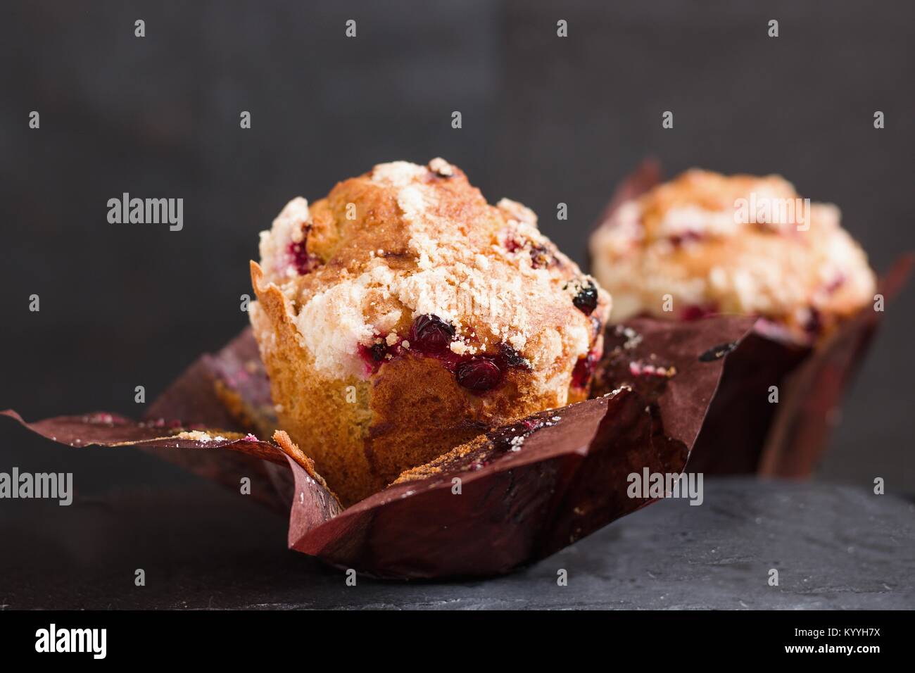 Due marrone carta avvolta di mirtilli rossi e uvetta muffin su sfondo scuro Foto Stock