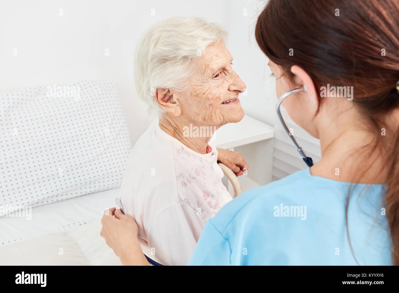 Il caregiver esamina vecchio paziente femmina con uno stetoscopio in casa di cura Foto Stock