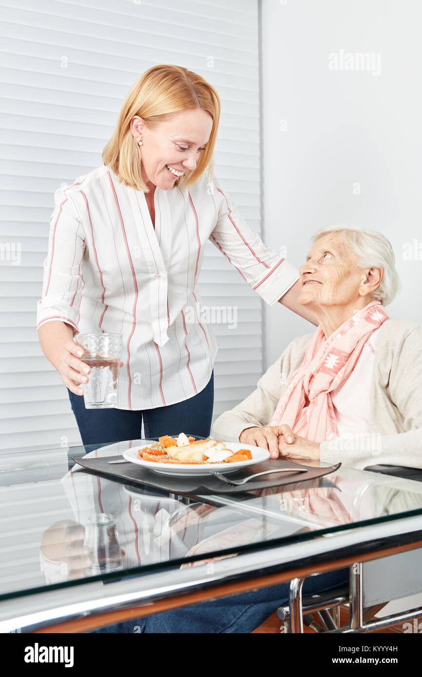 Giovane donna serve il pranzo per un senior a condizioni di vita assistita Foto Stock