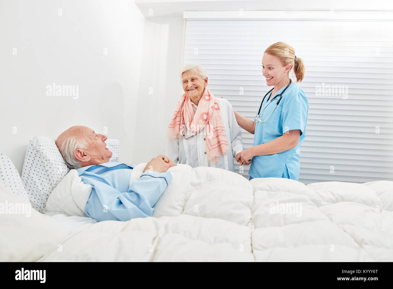 Senior come un paziente in ospedale ha una visita di sua moglie con l'aiuto di un assistente per allattamento Foto Stock