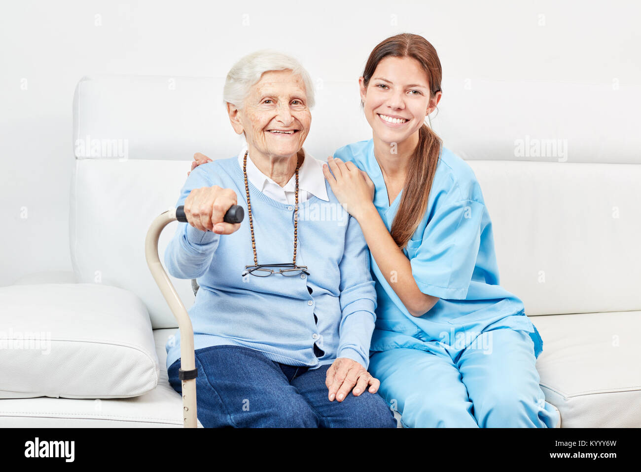 Sorridente donna infermieristica e felice donna anziana con walker sul divano Foto Stock