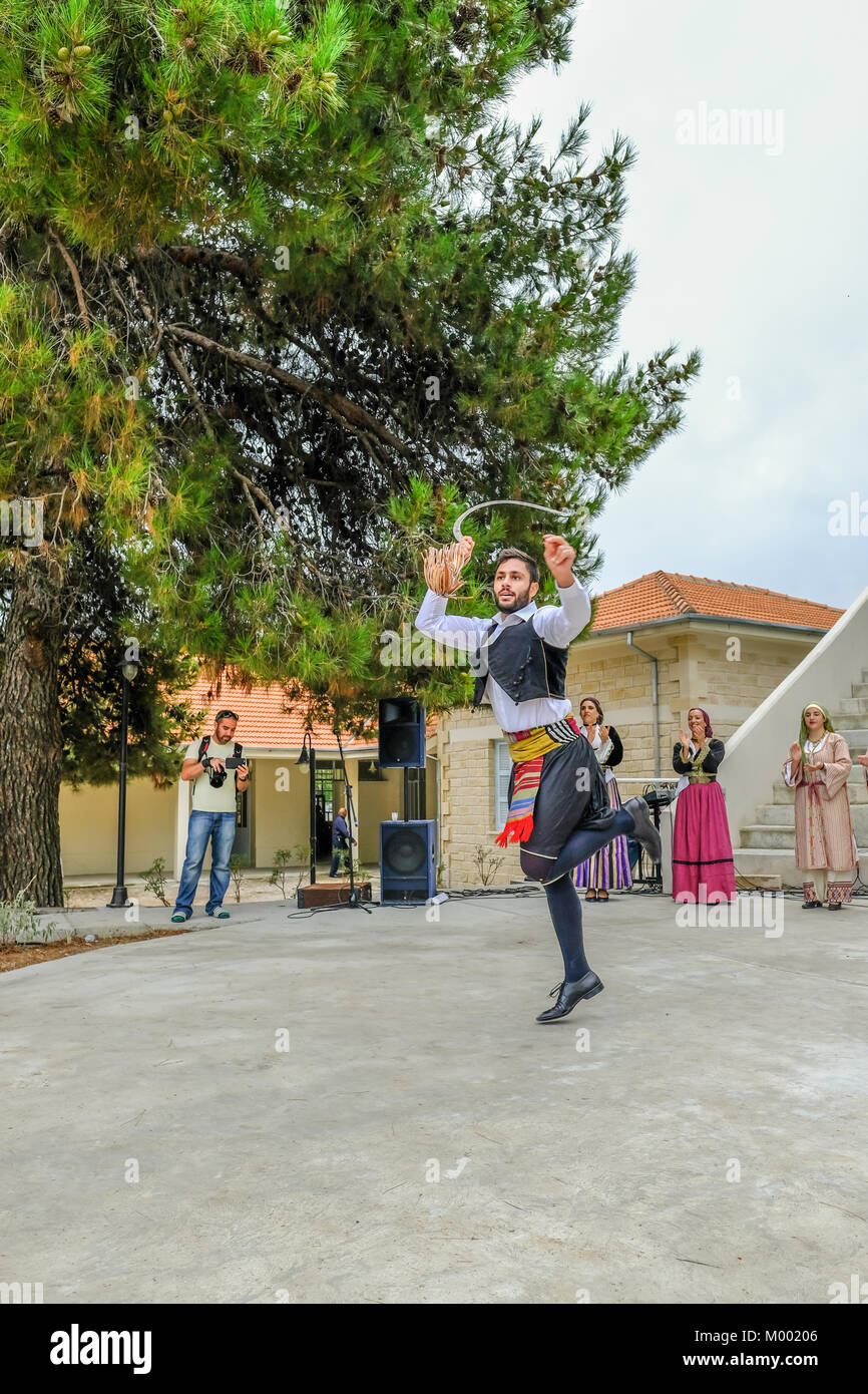 Villaggio Arsos, Cipro - 8 Ottobre 2017: uomo vestito in abiti tradizionali di eseguire il ballo folk, thrapani, holdng una falce, durante un festival. Foto Stock