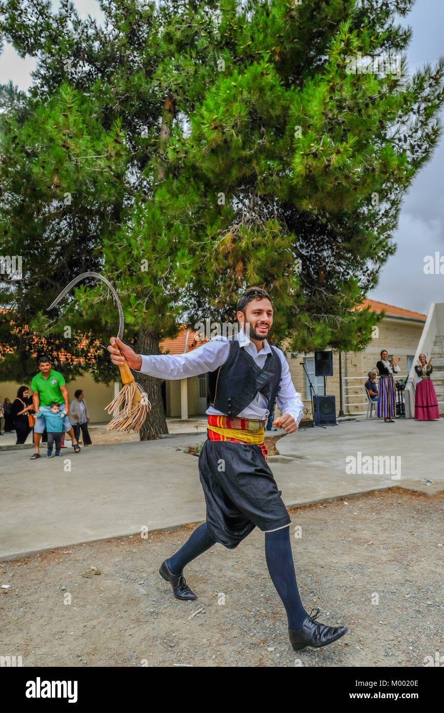 Villaggio Arsos, Cipro - 8 Ottobre 2017: uomo vestito in abiti tradizionali di eseguire il ballo folk, thrapani, holdng una falce, durante un festival. Foto Stock
