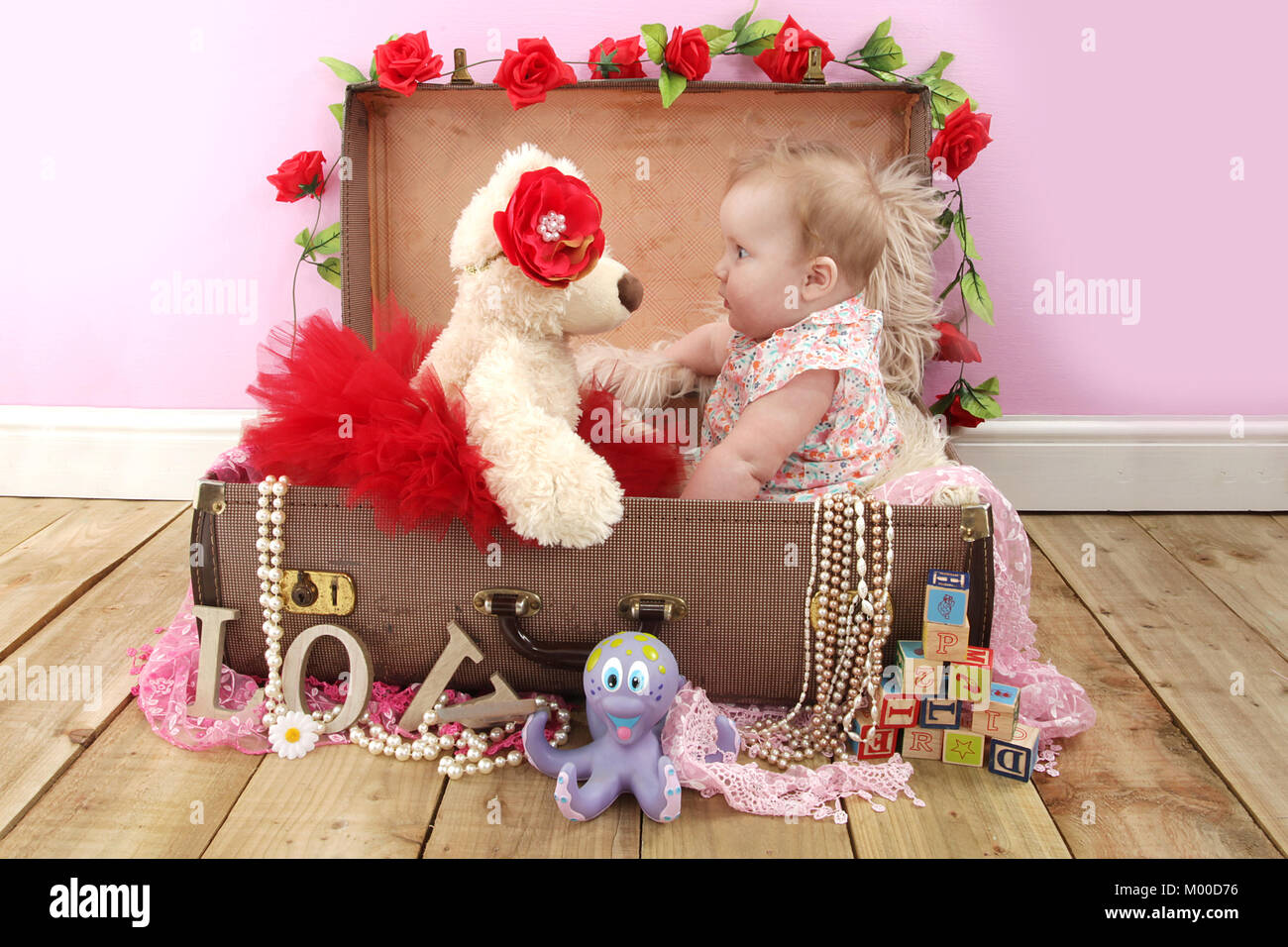 6 mese fa bella ragazza seduta con Teddy in una valigia, tempo di gioco nel vivaio Foto Stock