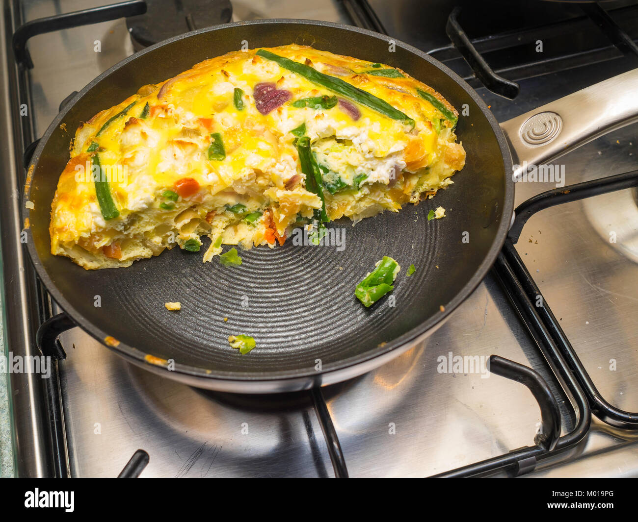 Una frittata fatta con uova e verdure cotte al forno su una padella padella  tagliato a metà per servire sul piano di cottura a gas Foto stock - Alamy