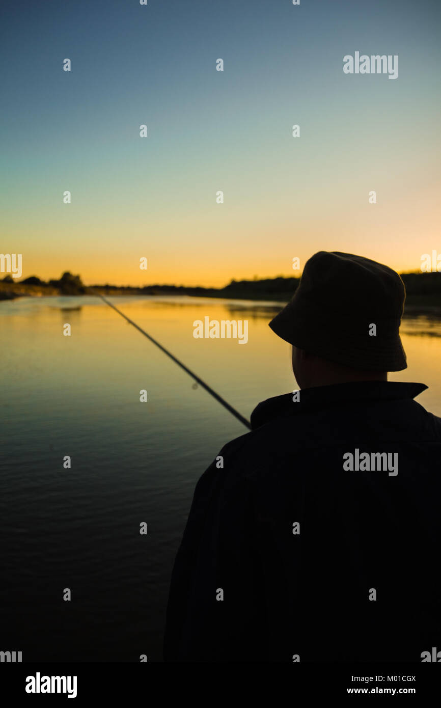 L'uomo pescatore con una canna da pesca seduti sulla riva del fiume nel  tempo al tramonto Foto stock - Alamy