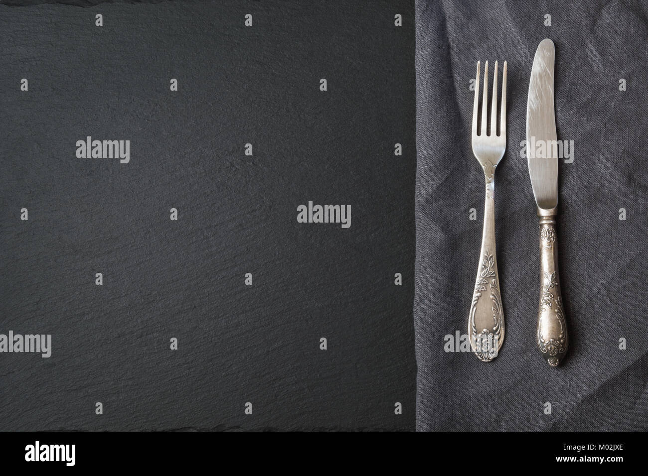 Rustico di lino grigio igienico, argenteria e nero ardesia piatto con copia spazio per il vostro menu o ricetta. Scheda del Menu per ristoranti. Vista dall'alto. Foto Stock