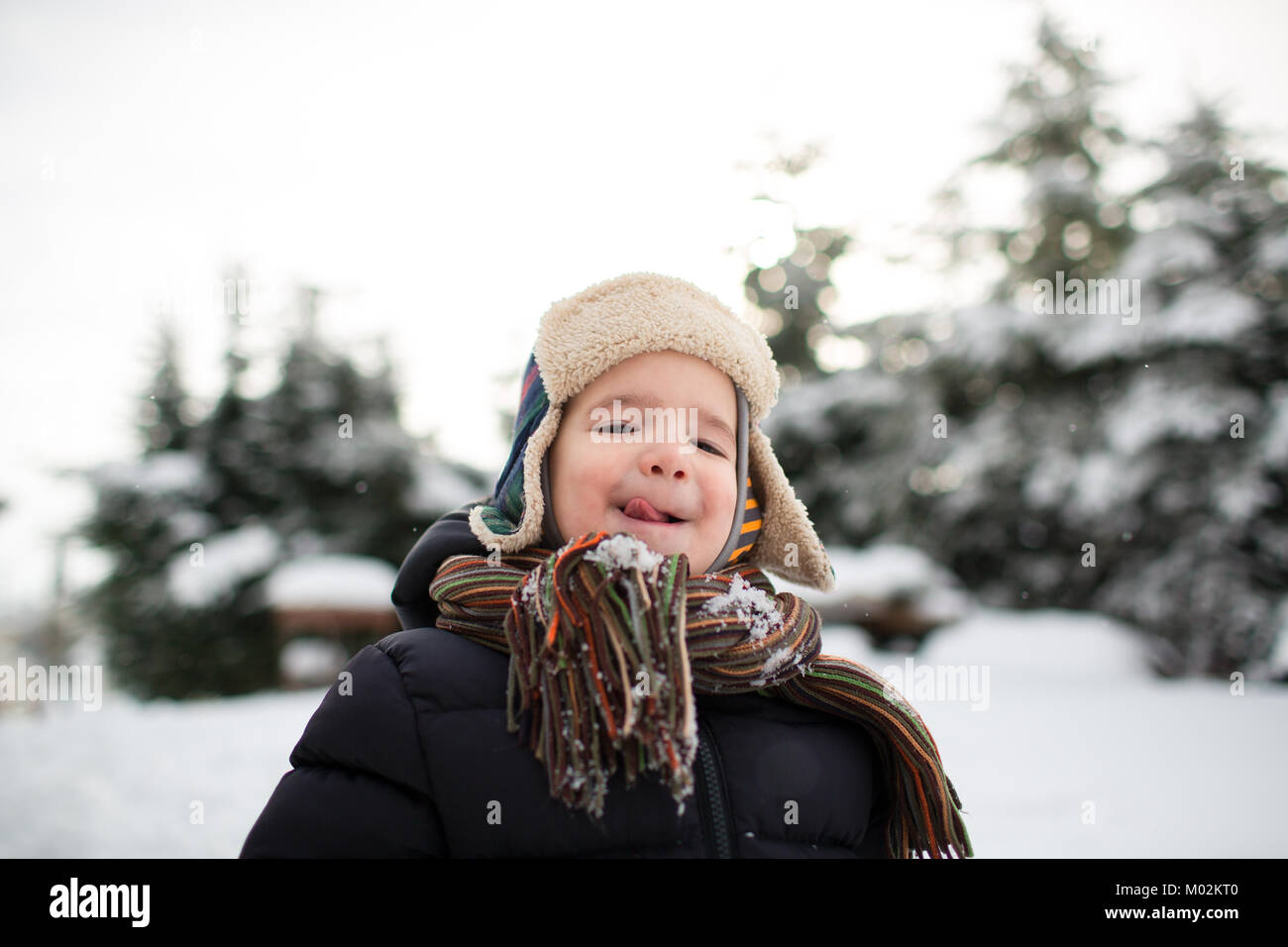 Bambino in vestiti caldi spuntavano una linguetta e la cattura dei fiocchi di neve. Ragazzo godendo di neve. Foto Stock