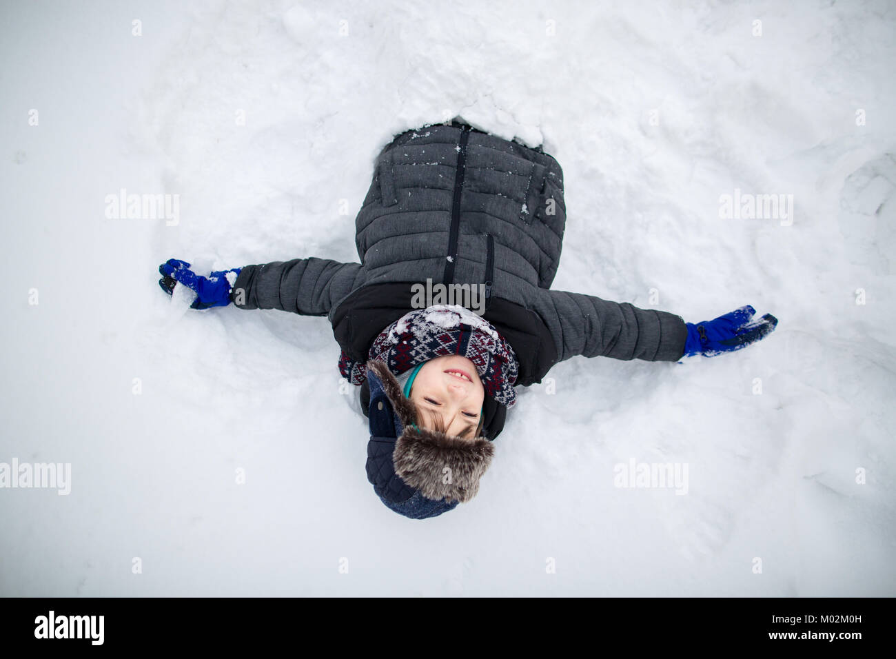 Elevato angolo di vista di un bambino sorridente nella neve con le sue braccia tese larghe. Ragazzo avente il divertimento sulla neve. Foto Stock