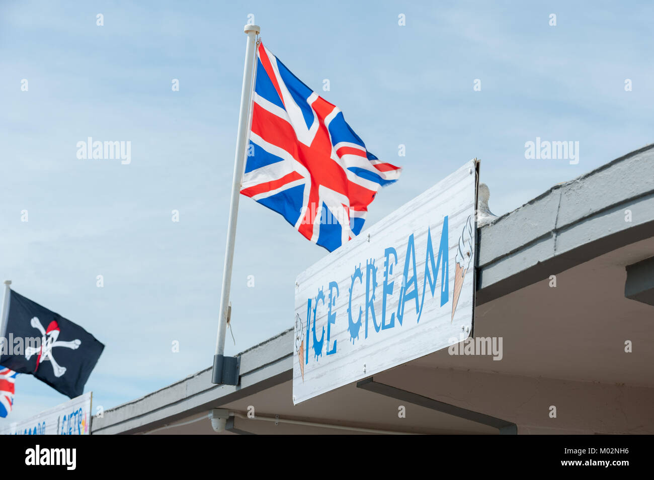 Un Union Jack flag sorvolando un gelato e segno contro un cielo blu su una giornata d'estate sul lungomare di Littlehampton, West Sussex. Foto Stock