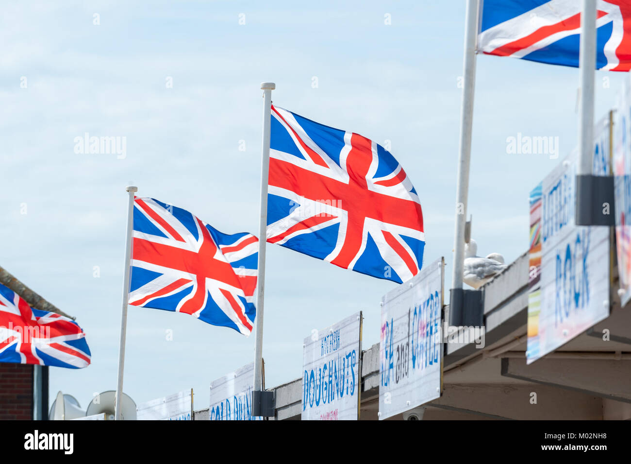 Unione Jack bandiere su fast food segni e contro un cielo blu su una giornata d'estate sul lungomare di Littlehampton, West Sussex. Foto Stock