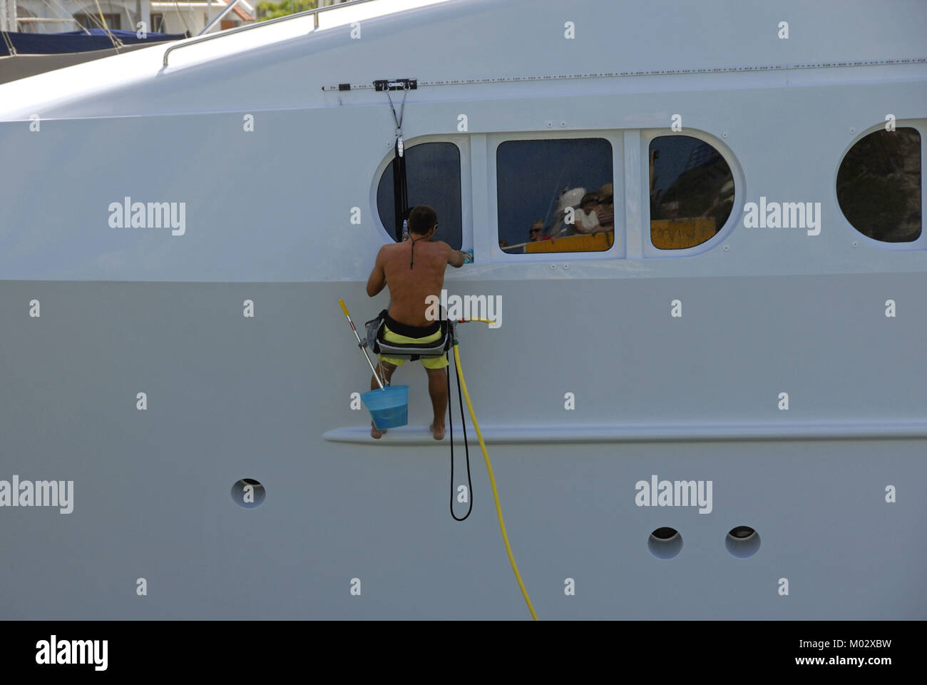 L'uomo sospesa sopra il lato del grande barca per pulirlo Foto Stock