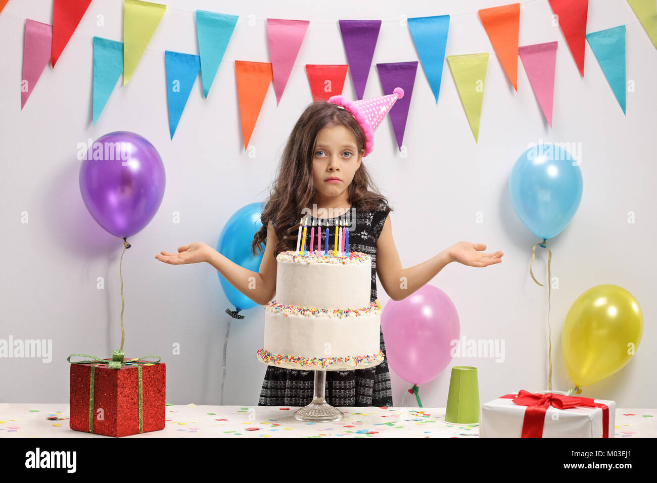 Delusa la ragazza con una torta di compleanno contro una parete con decorazione di bandiere e di palloncini Foto Stock