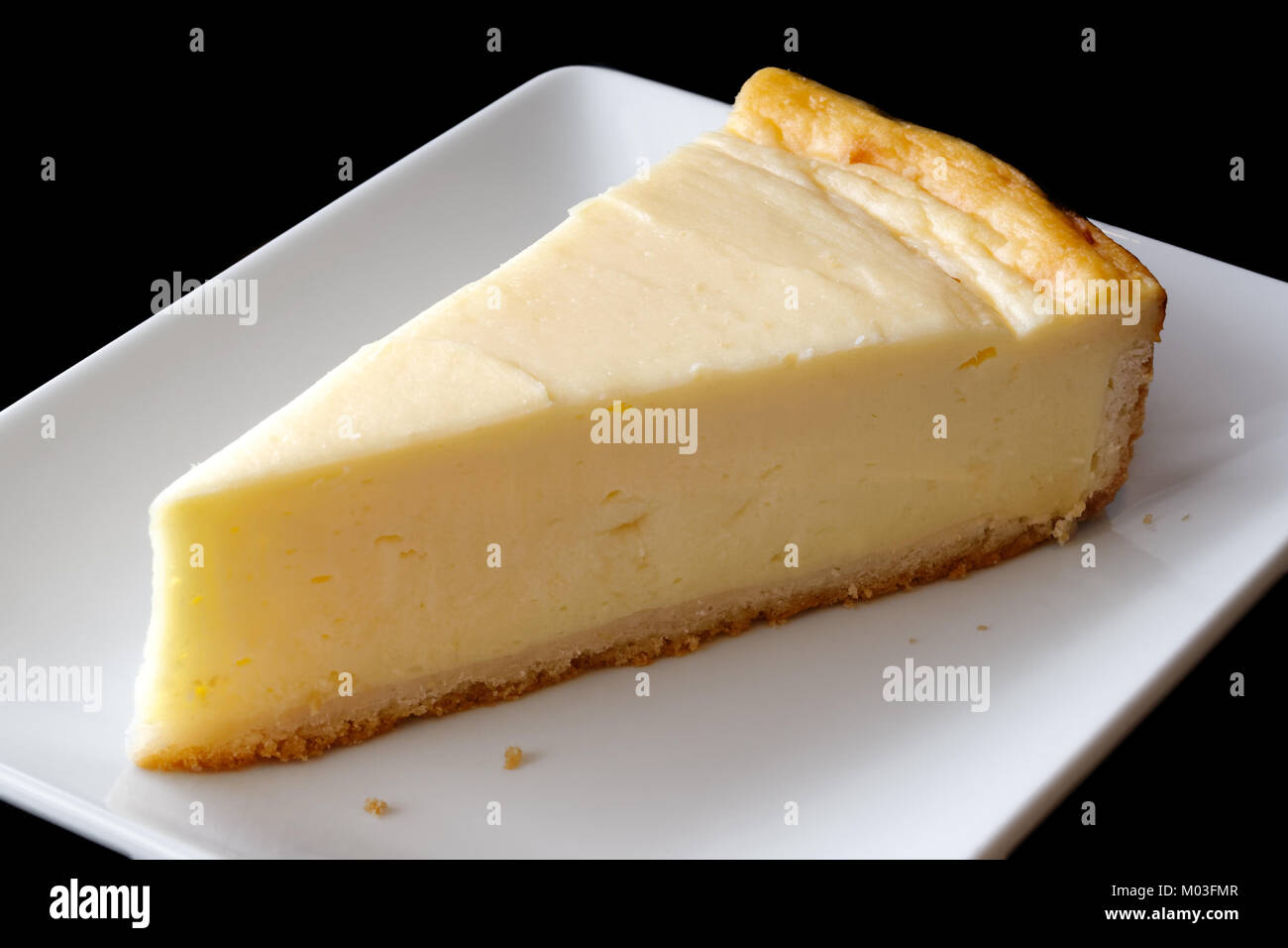 Una fetta della pianura cheesecake cotta sul piatto di portata in ceramica bianca. Sfondo nero. Foto Stock