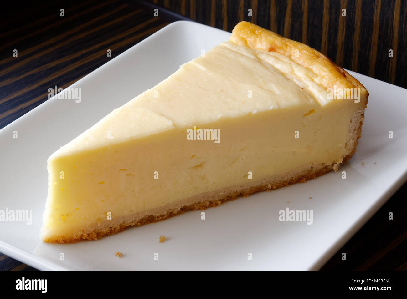 Una fetta della pianura cheesecake cotta sul piatto di portata in ceramica bianca. Sfondo scuro. Foto Stock