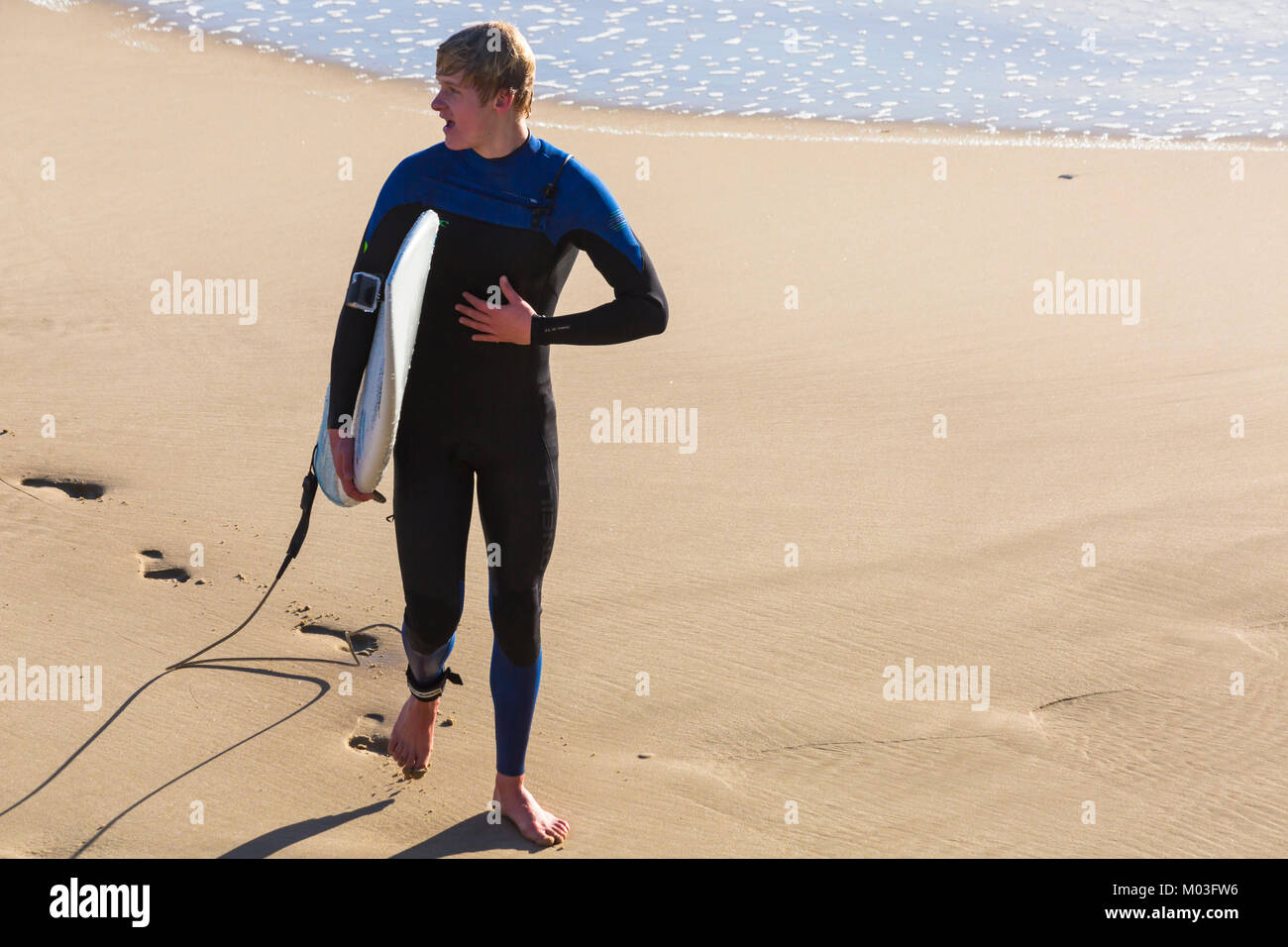 Surfer holding della tavola da surf camminando lungo la riva del mare a Bournemouth Beach e Bournemouth Dorset Regno Unito nel gennaio Foto Stock