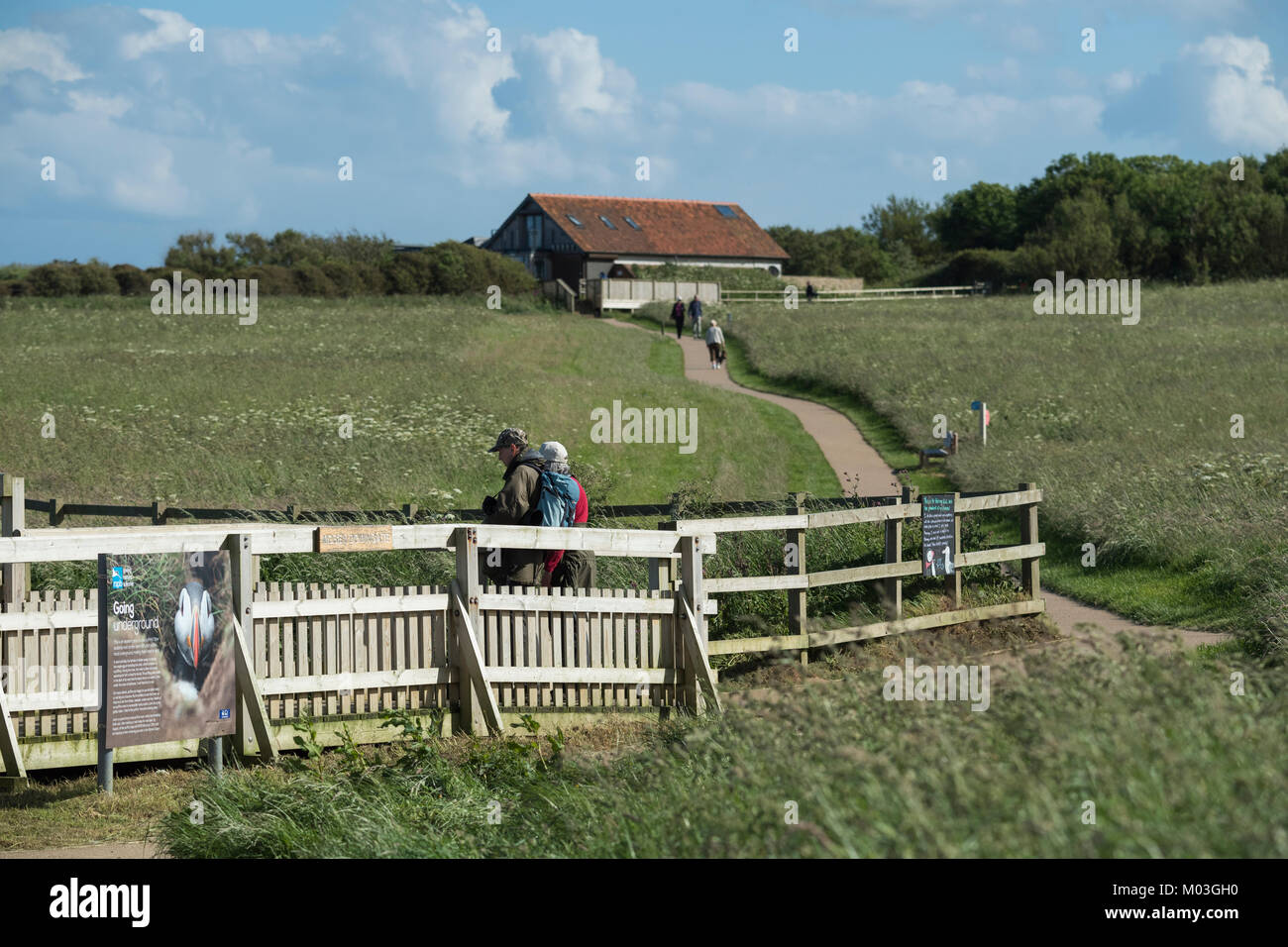 2 visitatori di RSPB riserva naturale stand al punto di visualizzazione mentre altre persone a piedi vicino al centro visitatori al di là - Bempton Cliffs, nello Yorkshire, Inghilterra, Regno Unito. Foto Stock