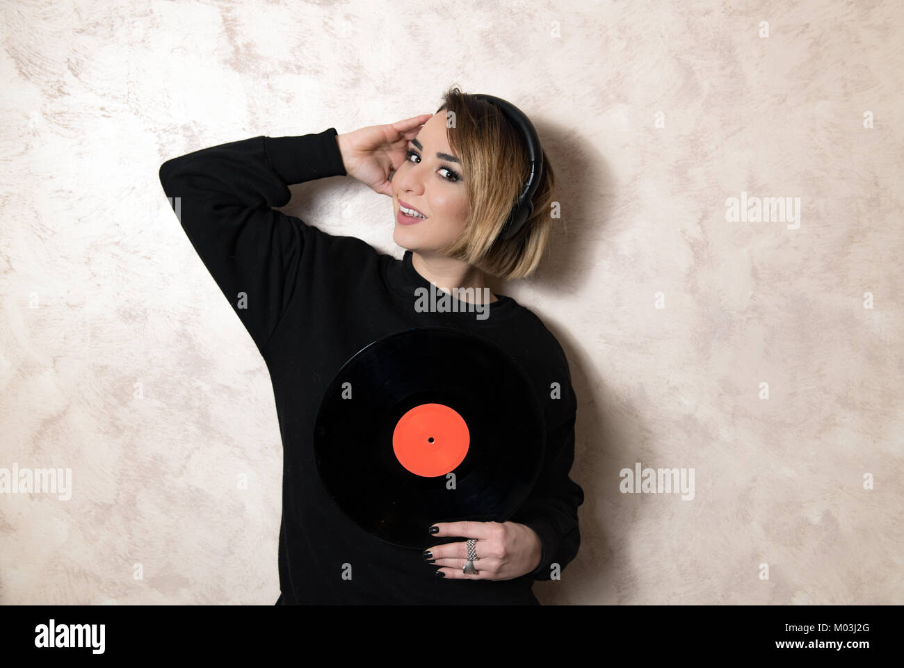 Bionda e giovane donna graziosa con cuffie guardando la telecamera con l'annata record del vinile lungo la riproduzione nelle sue mani Foto Stock