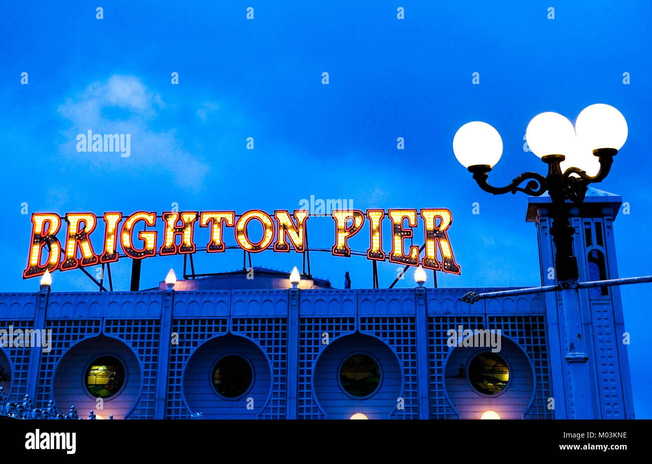 Il Brighton Pier rosso brillante e neon giallo segno dicendo il Brighton Pier, sullaparte superiore del Molo di Brighton ingresso con una lampada di strada dietro, scattata di notte, blu hu Foto Stock