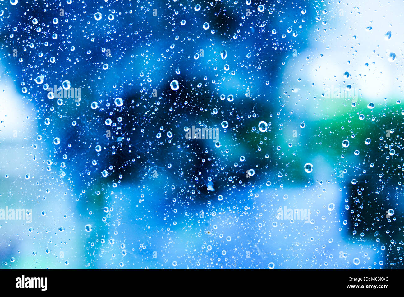 Centinaia di bianco delle gocce di pioggia su una finestra di vetro con uno sfondo sfocato di blu, verde e bianco colori di tonalità variabile Foto Stock