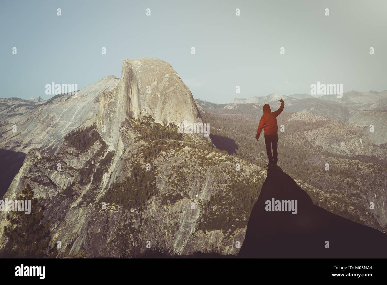 Un giovane escursionista è in piedi su una roccia godendo della vista verso il famoso Half Dome presso il Glacier Point in beautiful Golden luce della sera al tramonto in estate Foto Stock