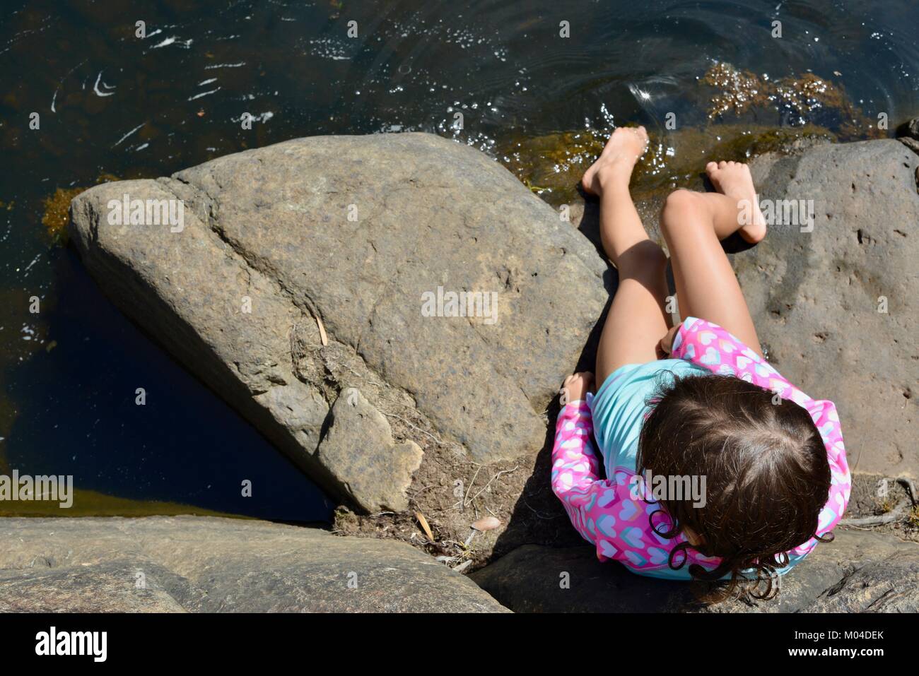 Bambino seduto sulle rocce accanto a un fiume fotografato dal di sopra, Bowling Green Bay National Park (Alligator Creek), Townsville, Queensland, Australia Foto Stock