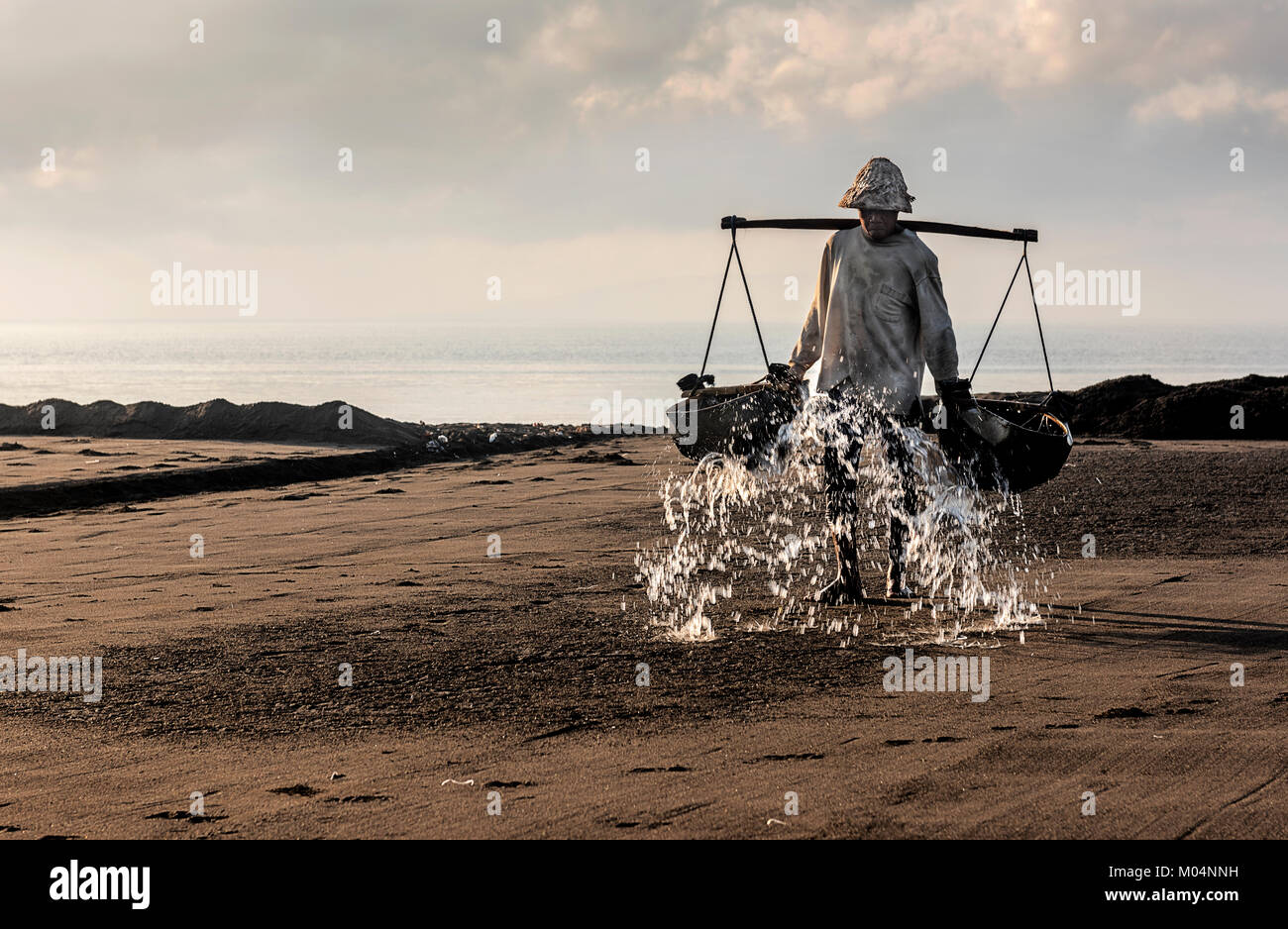 Sale indonesiano agricoltore di Kusamba sale villaggio minerario di Bali la raccolta di acqua di mare al mattino per la produzione di sale utilizzando il metodo tradizionale Foto Stock