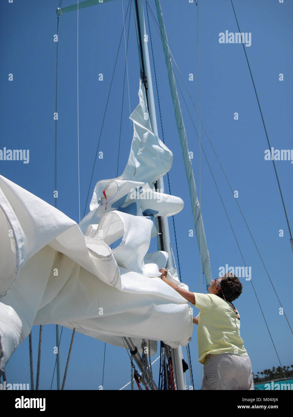 Questa fotografia, "Bringing in the Sail", cattura il momento in cui la vela di una barca a vela viene portata qui. L'immagine illustra le tecniche di navigazione e cattura le dinamiche della navigazione durante una gara o un'attività di routine sull'acqua. Foto Stock