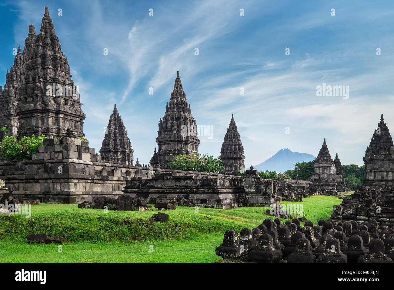 Antiche rovine di pietra sul campo verde e Candi Prambanan o Rara Jonggrang, tempio indù composto sullo sfondo. Impressionante architettura sito. Yogyakar Foto Stock