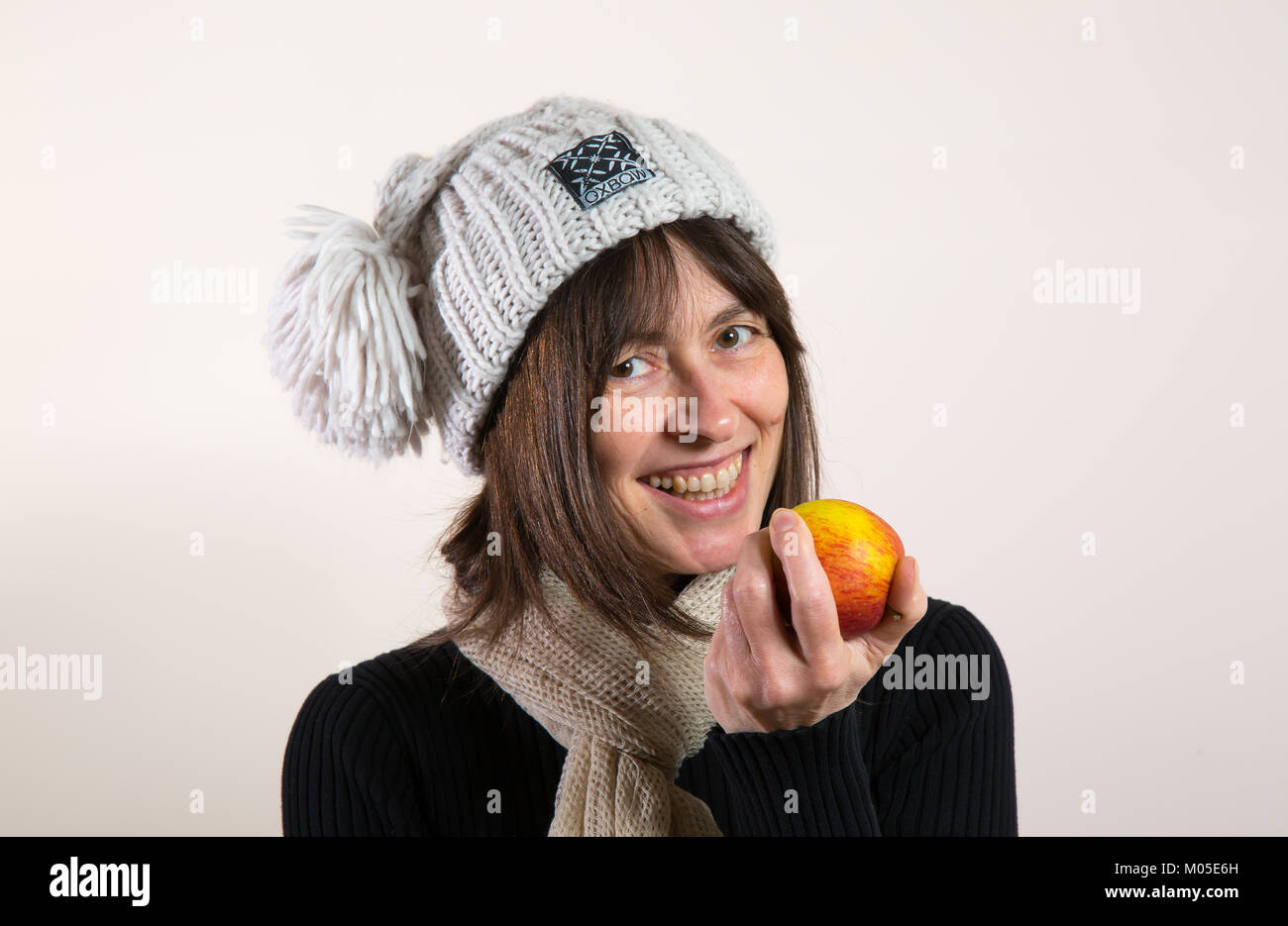 Ritratto interno, felice sana e isolata ragazza sorridente, in bobble cappello, tenendo in mano mela fresca pronta a prendere un morso. Bel sorriso naturale grande. Foto Stock