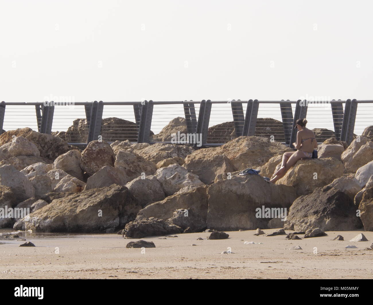 La donna siede sulla spiaggia spiaggia di roccia su un perfetto giorno chiaro Foto Stock