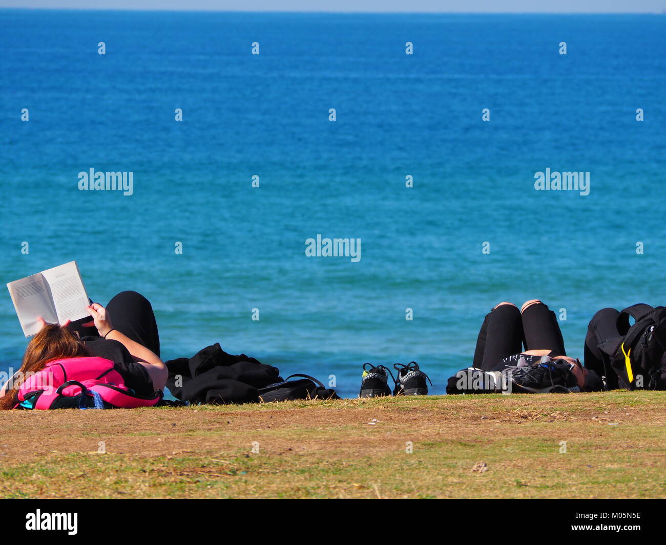 Gruppo di amici sdraiati al sole e relax divertimento presso il lungomare vicino alla spiaggia di fronte al mare su una giornata perfetta con cielo blu chiaro Foto Stock