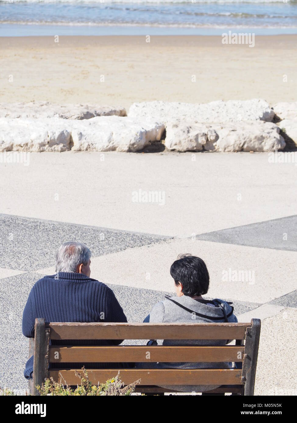 Un senior giovane seduto sulla spiaggia di sabbia in una perfetta giornata limpida e guardare il mare Foto Stock