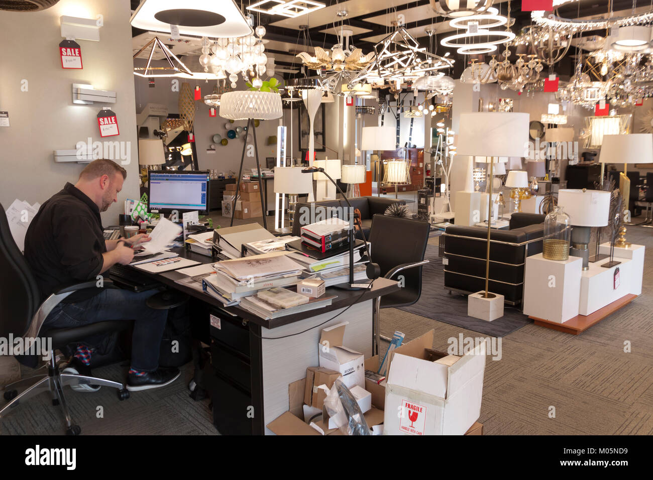 Un dipendente che lavora presso la sua scrivania entro una illuminazione di retail store. Foto Stock