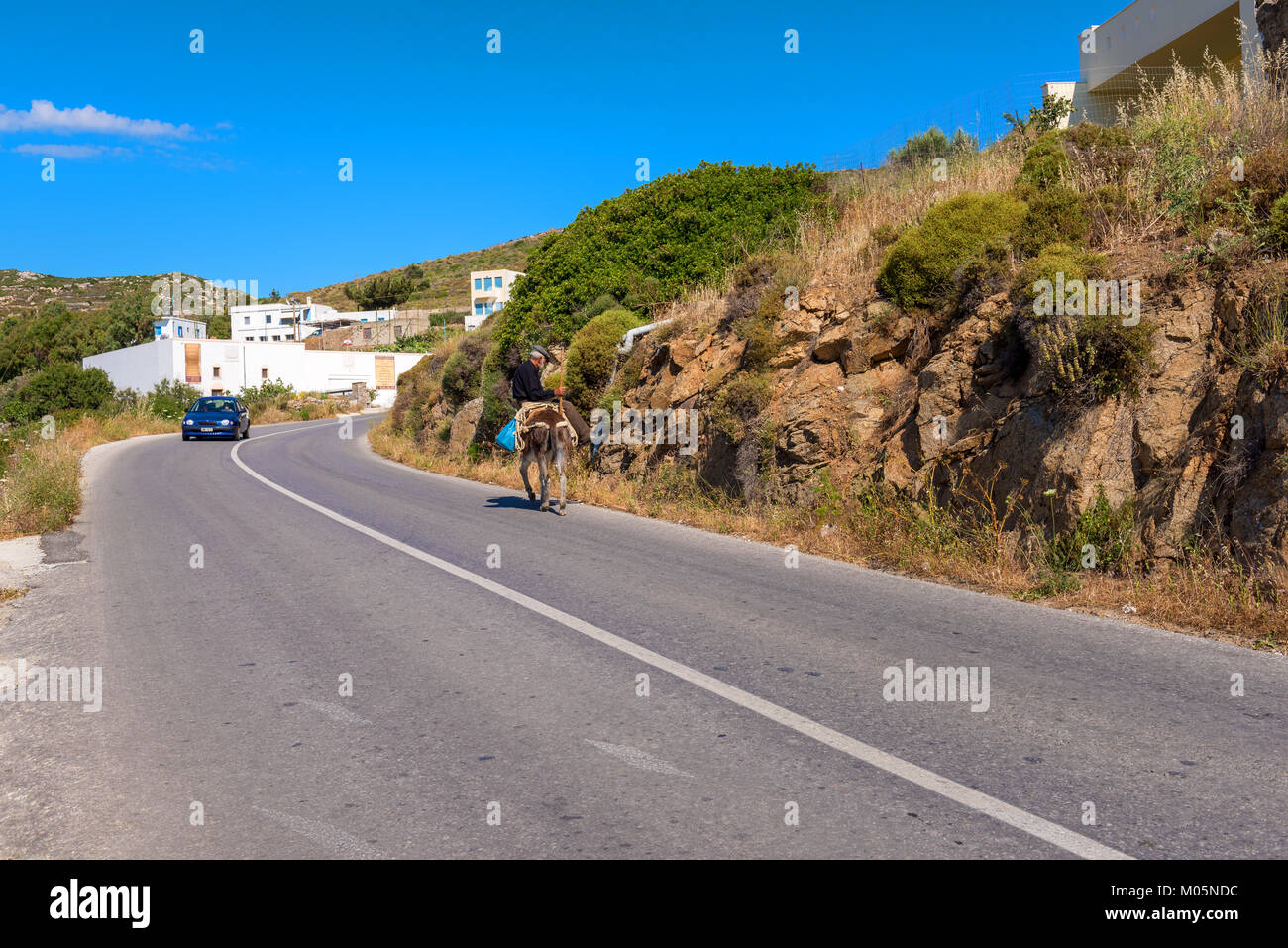 NAXOS, Grecia - 24 Maggio 2017: il vecchio uomo che cavalca un asino sulla strada a isola di Naxos. Foto Stock