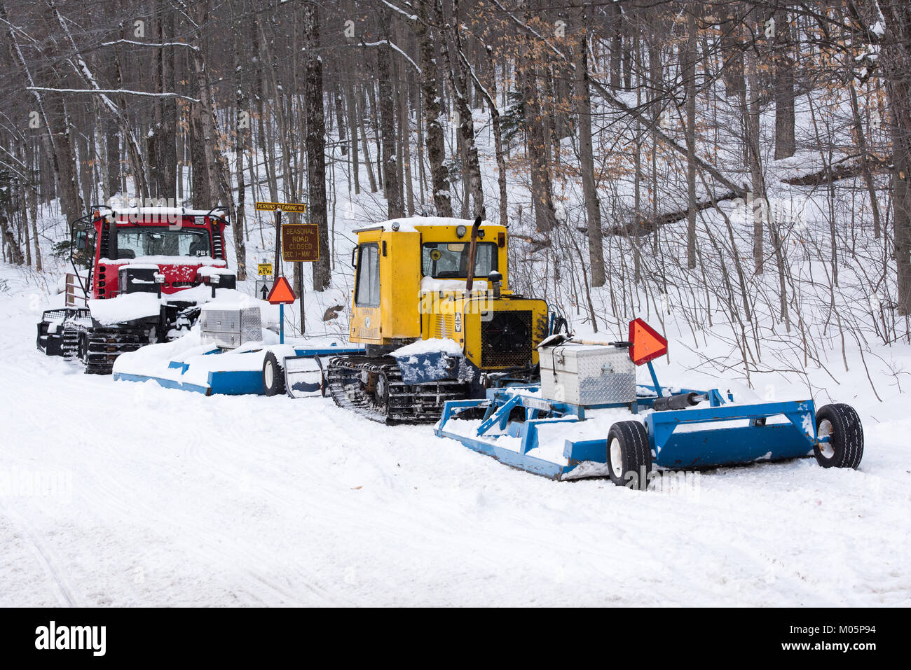 Due snowmobile trail groomers, un giallo Bombardier e un rosso pisten bully, parcheggiato su un motore Perkins a compensazione di strada nella Adirondacks. Foto Stock