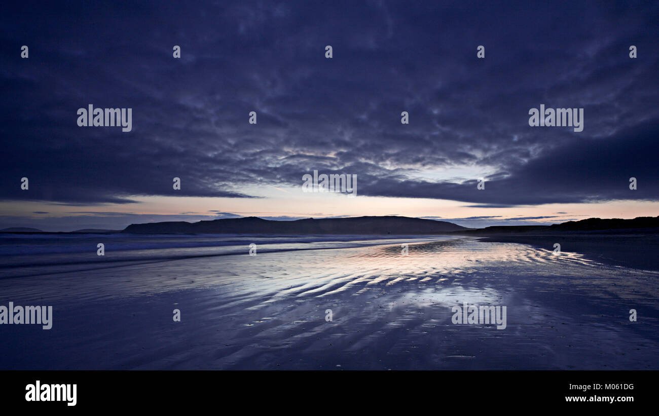 Nuvole drammatico al tramonto riflettendo sulla sabbia bagnata Foto Stock