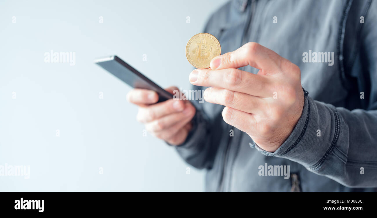 Uomo con bitcoin e il telefono cellulare, la stretta di mano con BTC cryptocurrency moneta e lo smartphone Foto Stock