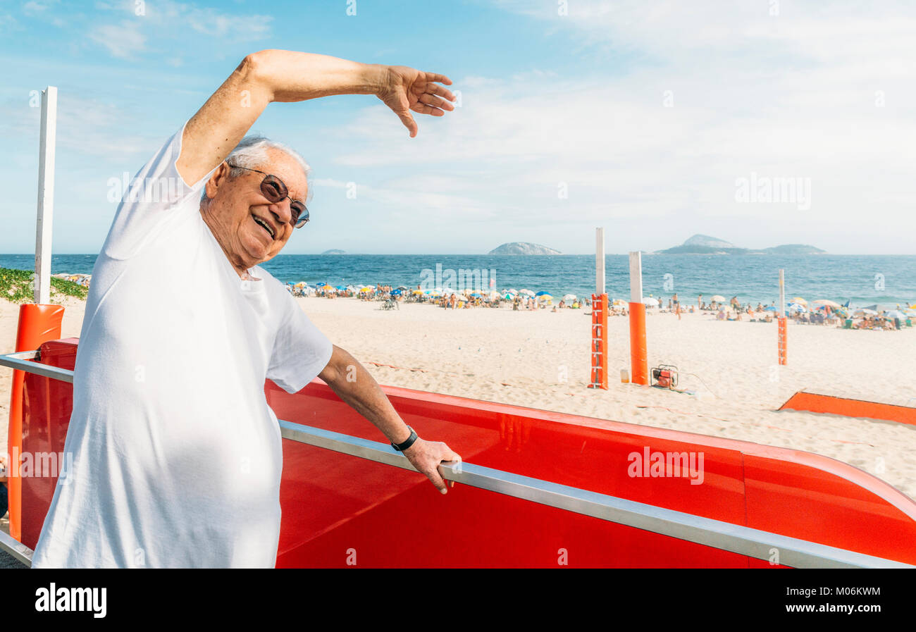 Modello rilasciato - uomo anziano sorrisi durante lo stiramento affacciato sulla spiaggia di Ipanema a Rio de Janeiro in Brasile Foto Stock