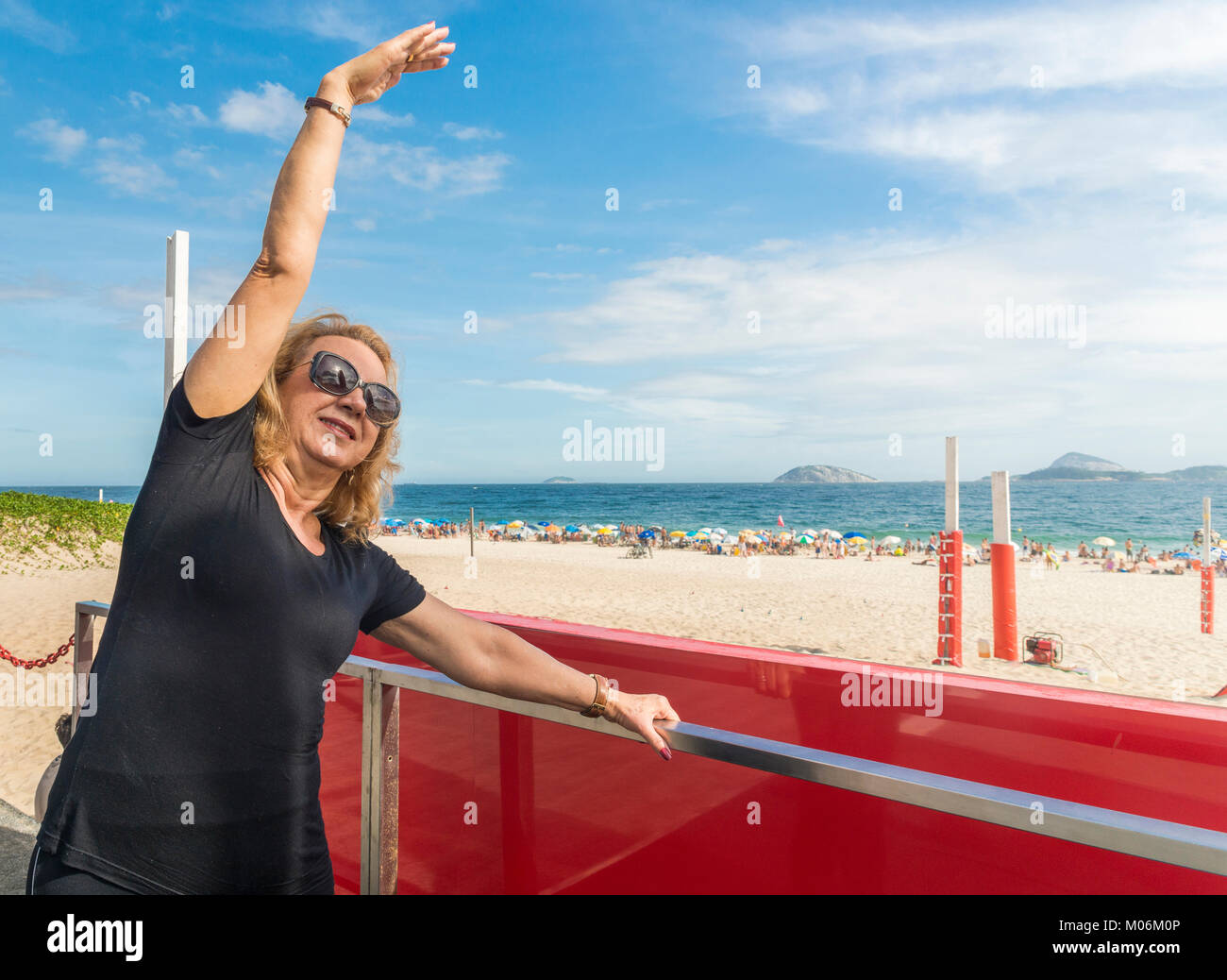 Modello rilasciato - donna anziana sorrisi durante lo stiramento affacciato sulla spiaggia di Ipanema a Rio de Janeiro in Brasile Foto Stock