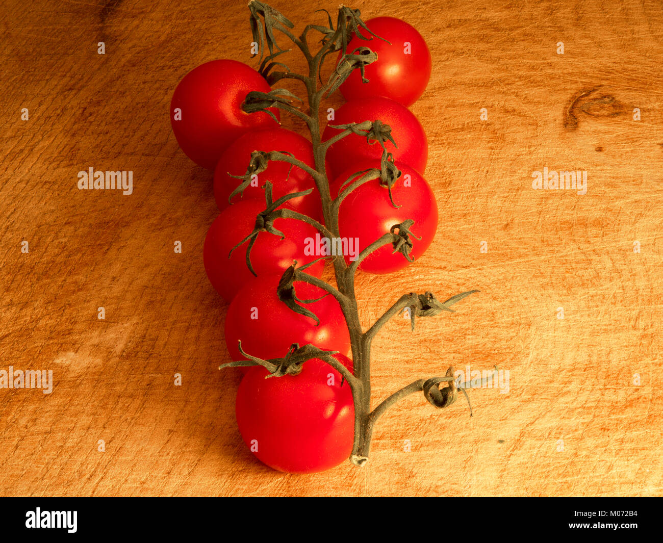 Miniatura pomodori ciliegia sulla vite su un tagliere Foto Stock