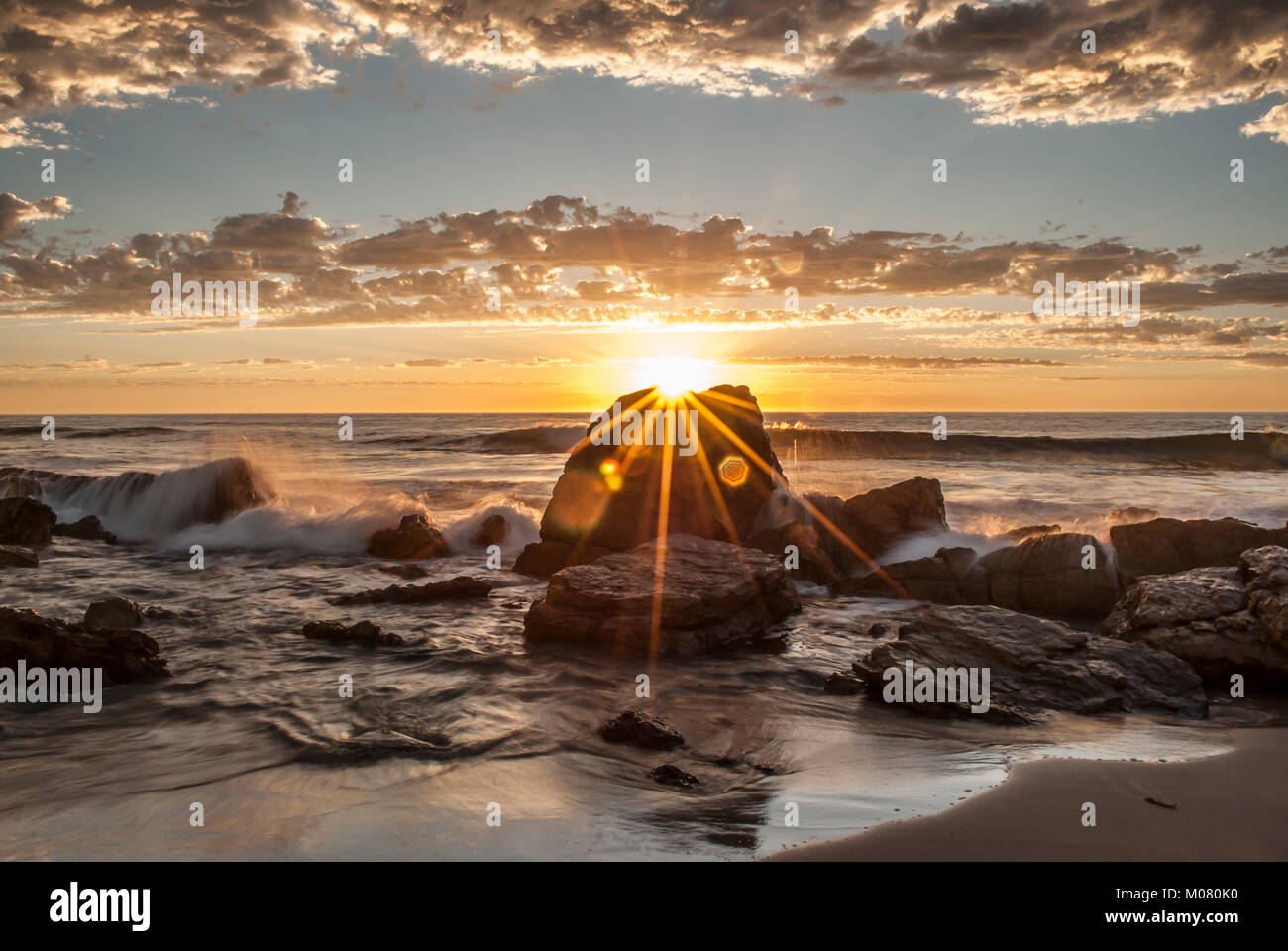 Un burst di sole al tramonto O'Sullivan Beach, Sud Australia, completo di irrorazione di acqua, le onde del mare Foto Stock