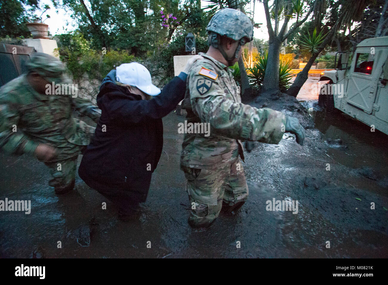 Sgt. Jose Paiz, destra e Staff Sgt. Michael Aguilar, a sinistra, entrambi del composito 1114th Truck Company, California Guardia nazionale, guida una donna attraverso dense knee-fango profondo Gen 12, 2018 da un Montecito, California, la Casa del Soldato' Humvee. Il 1114th è accreditato con il salvataggio o evacuazione di più di 1.800 persone nella zona Montecito a seguito di una frana di fango mortale che ha colpito la città nel predawn ore gen. 9. (Air National Guard Foto Stock