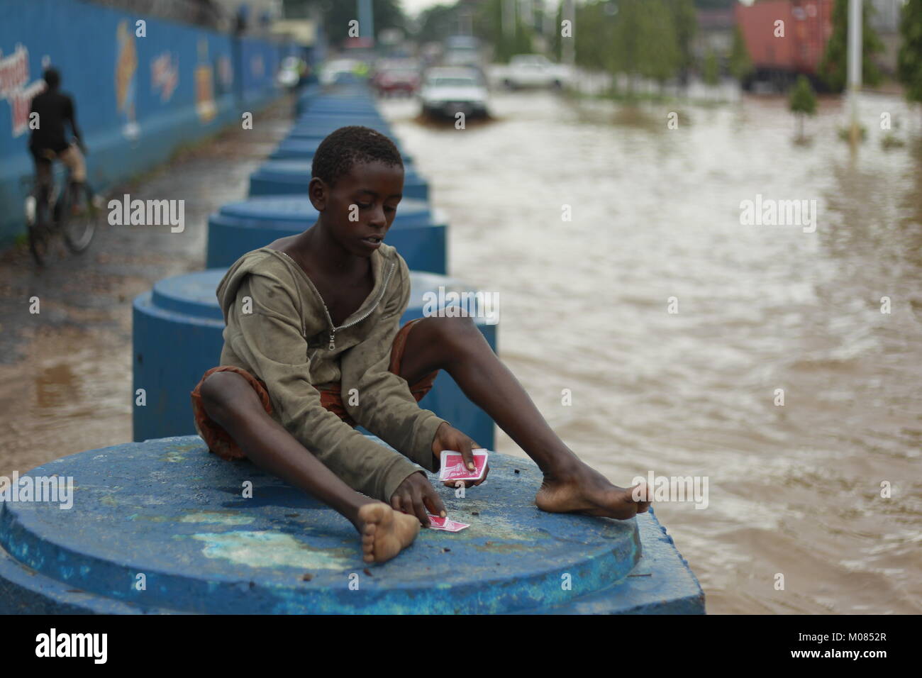 Un ragazzo si siede a giocare a carte da sola su un blocco di cemento durante un diluvio di Bujumbura capitale del Burundi Foto Stock