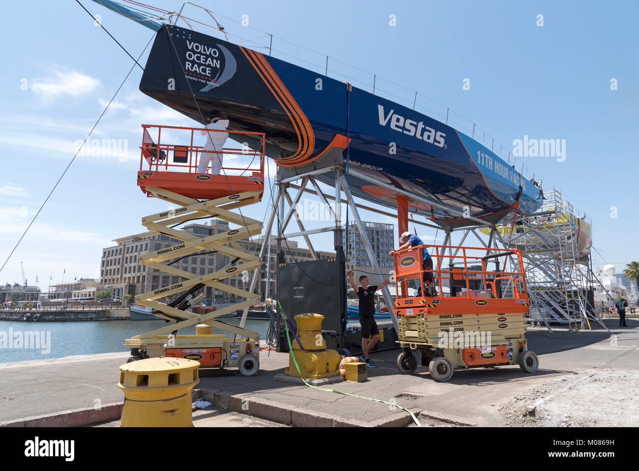 Cape Town Waterfront Sud Africa. Dicembre 2017. Volvo Ocean Race. Racing yacht Vestas. La lucidatura dello scafo da parte dei membri del team utilizzando sollevatori a forbice Foto Stock