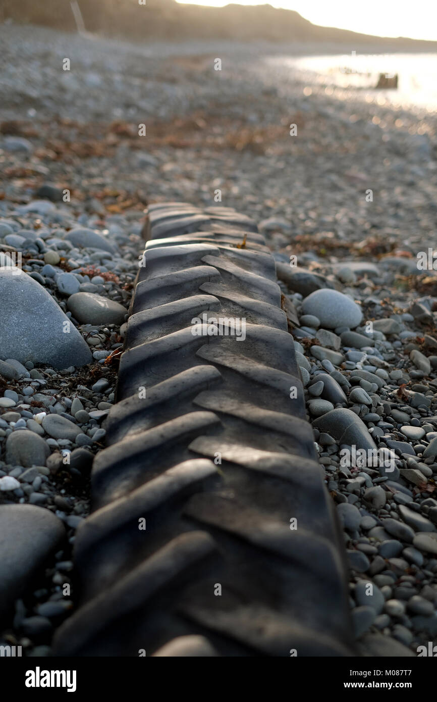 Il pneumatico del trattore abbandonato al mare si siede sulla spiaggia in attesa della prossima alta titde Foto Stock