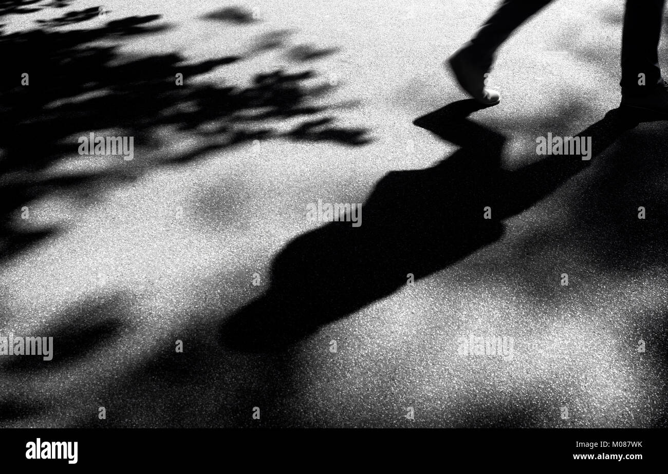 Sfocata ombra silhouette di un uomo a camminare da sola nel parco della città in bianco e nero Foto Stock