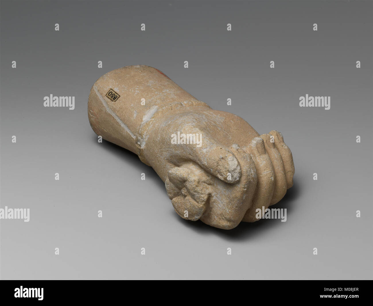 Questo frammento di statua in pietra calcarea raffigura una mano destra che tiene un fiore e indossa un bracciale, esemplificando l'arte classica nella collezione MET. Foto Stock