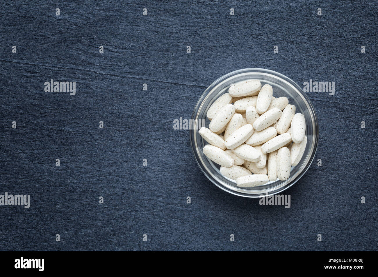 Piccola ciotola di vetro riempito con complessi multivitaminici contro una pietra scura sullo sfondo Foto Stock